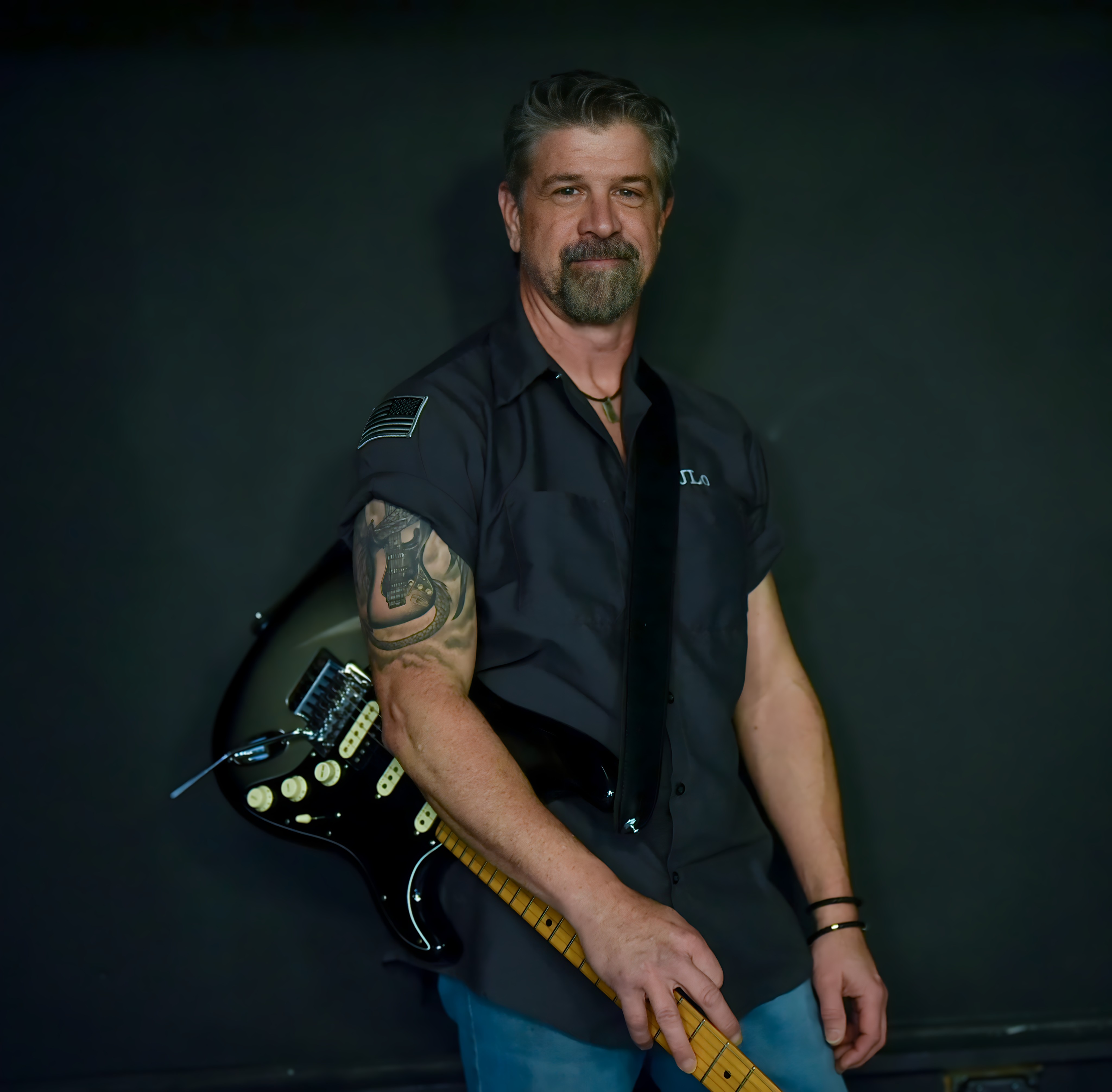 Joe in a dark short-sleeved shirt with his guitar