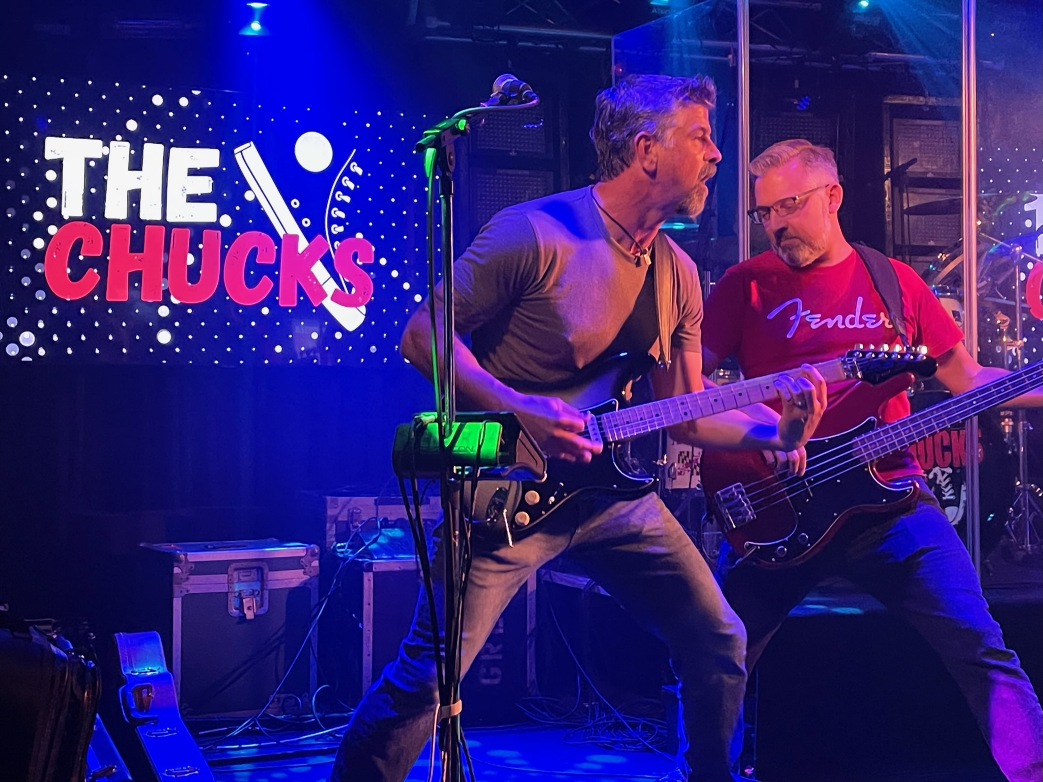Guitar and bass players leaning into a song under blue and purple stage lights