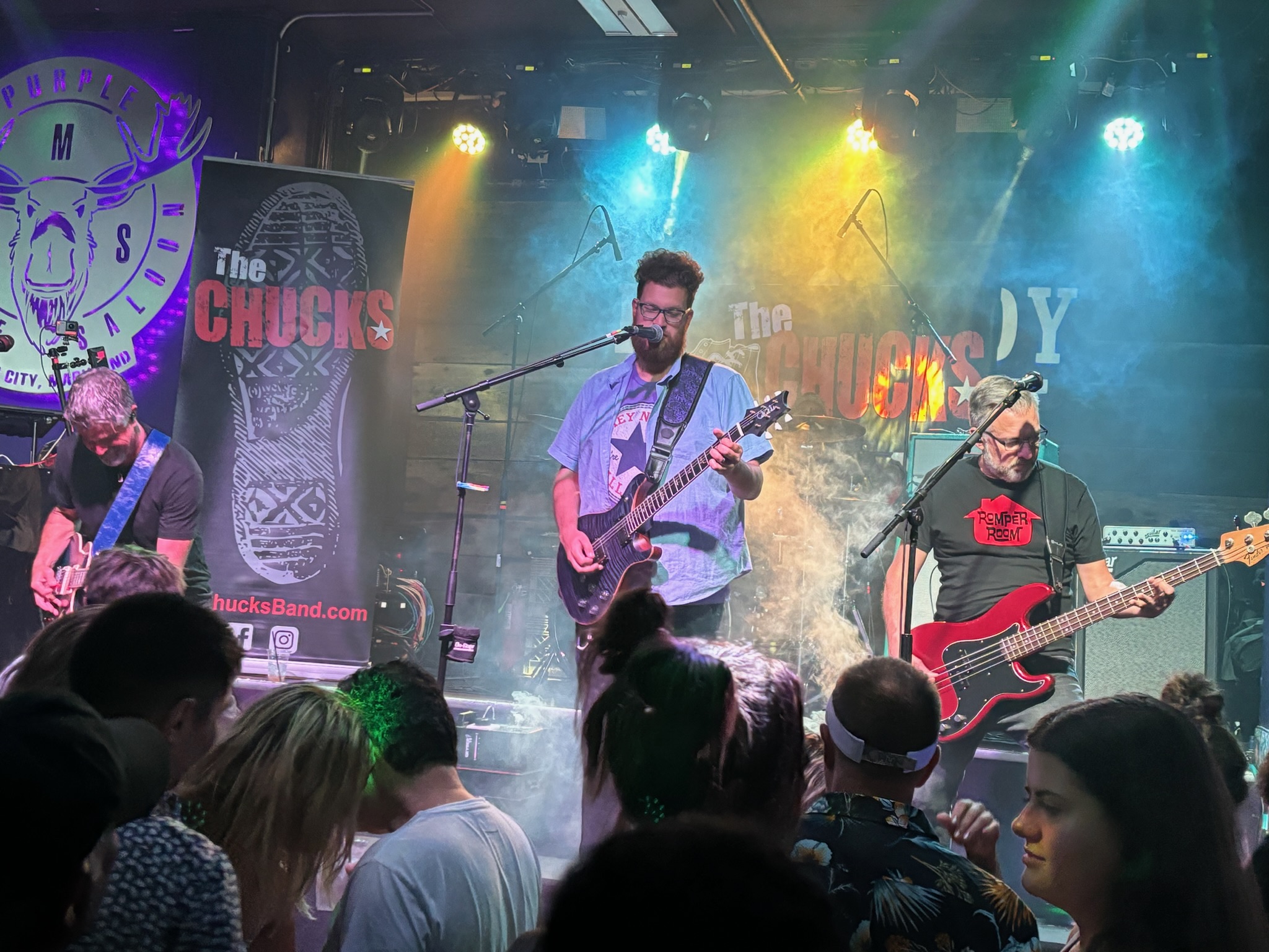 The Chucks performing above a close-packed crowd under cyan and gold lights at the Purple Moose