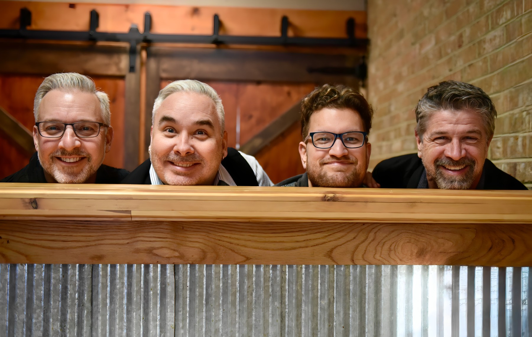 The four members of The Chucks smiling over the edge of a wooden bar