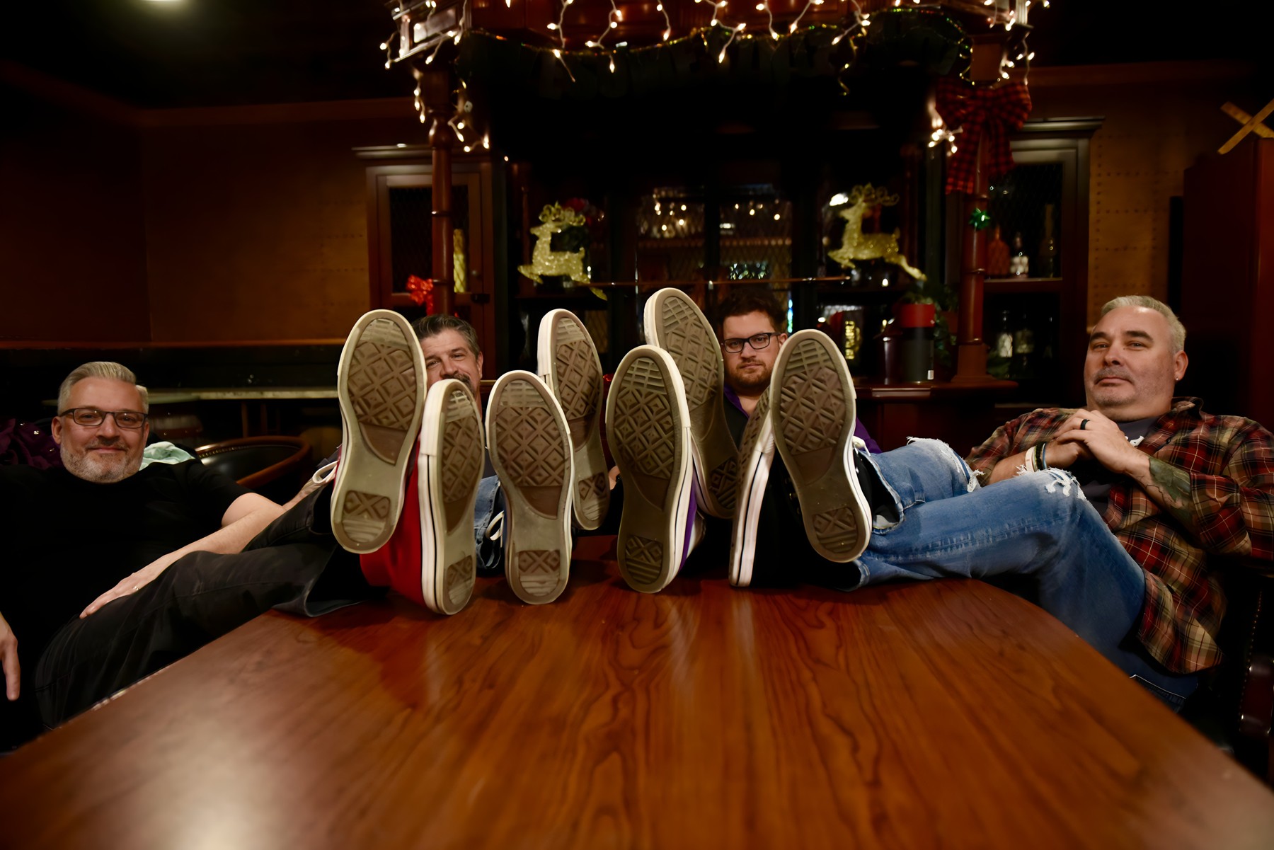 The four band members leaning back with their colorful Chucks up on a table