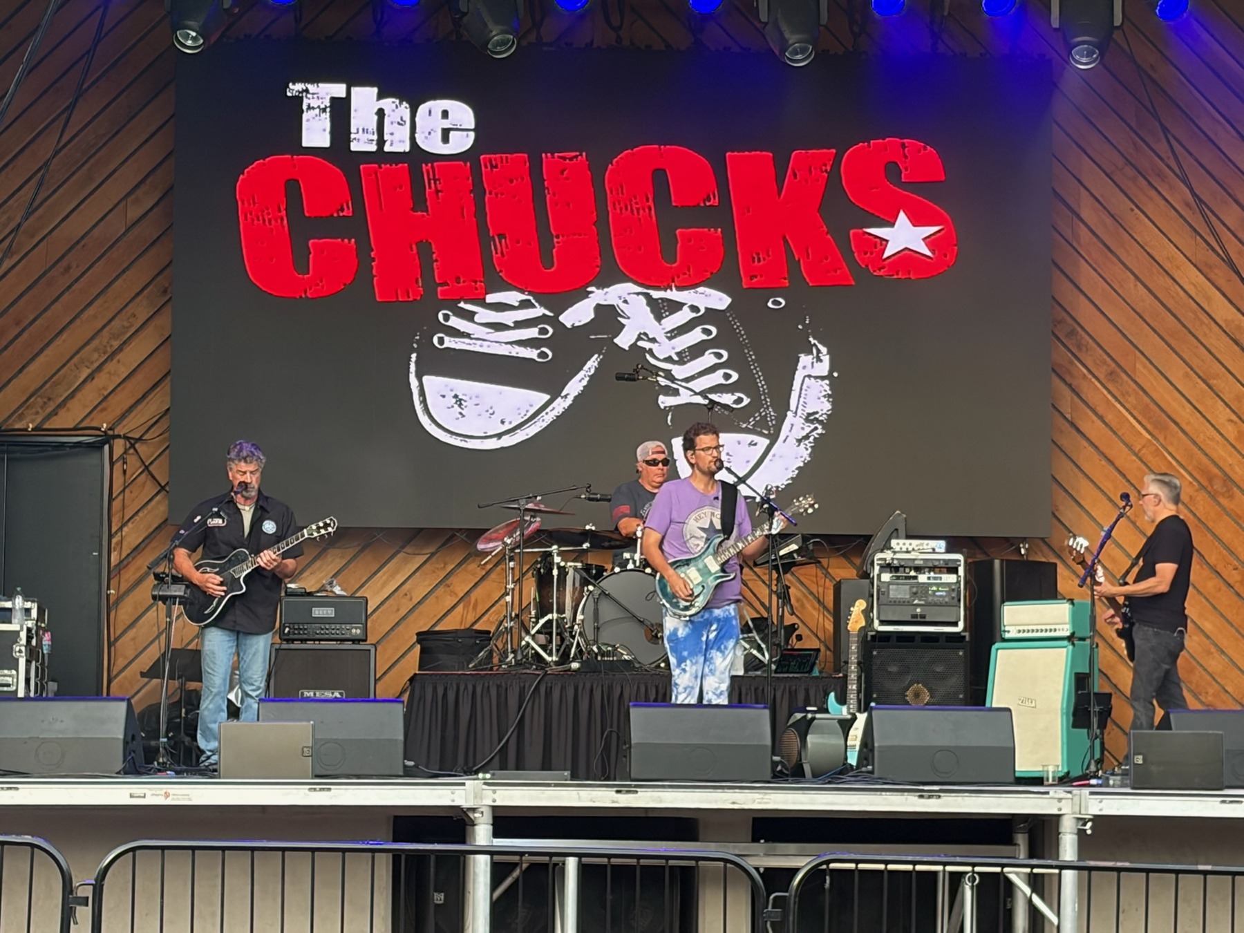 The Chucks performing together beneath their large red and white logo on a wood-paneled stage