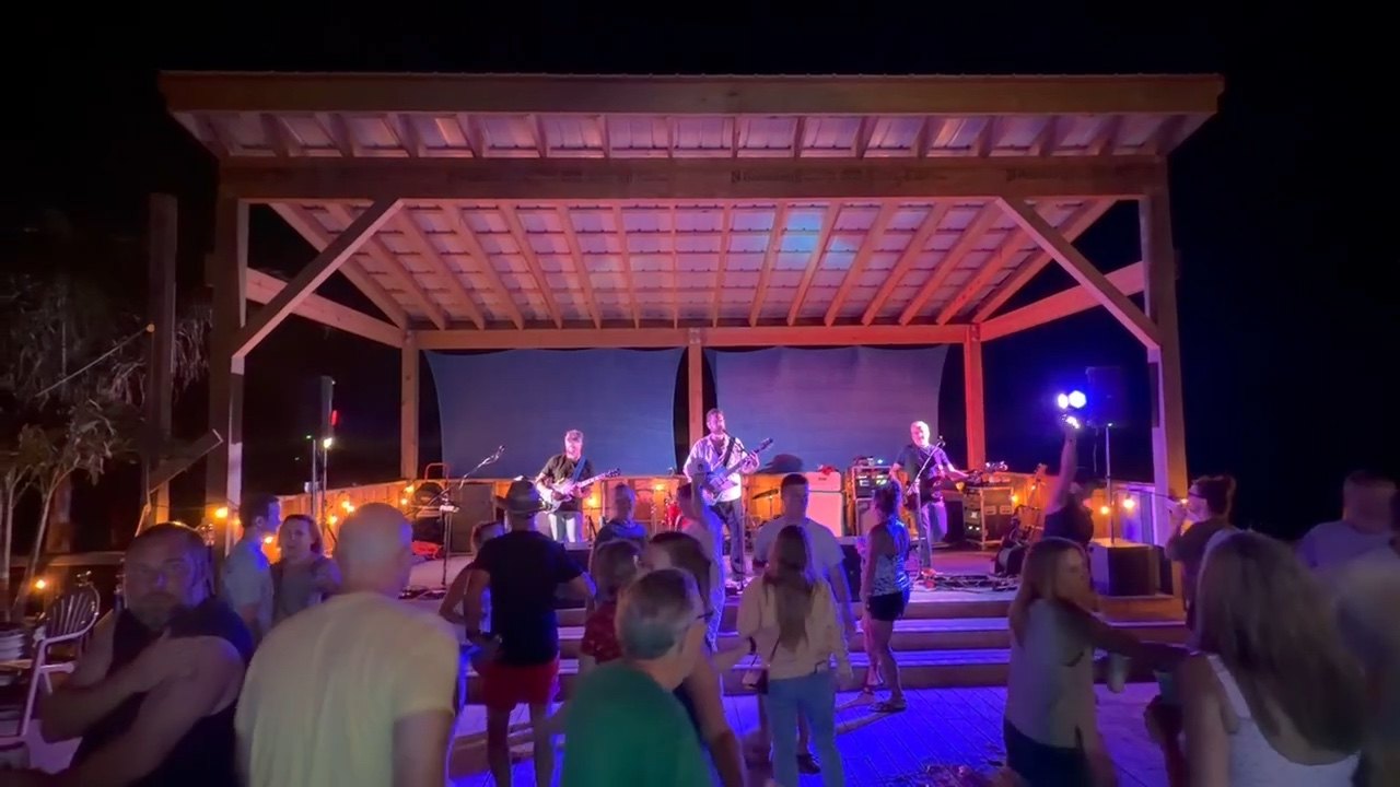 People dancing in front of The Chucks on an open-air waterfront stage after dark