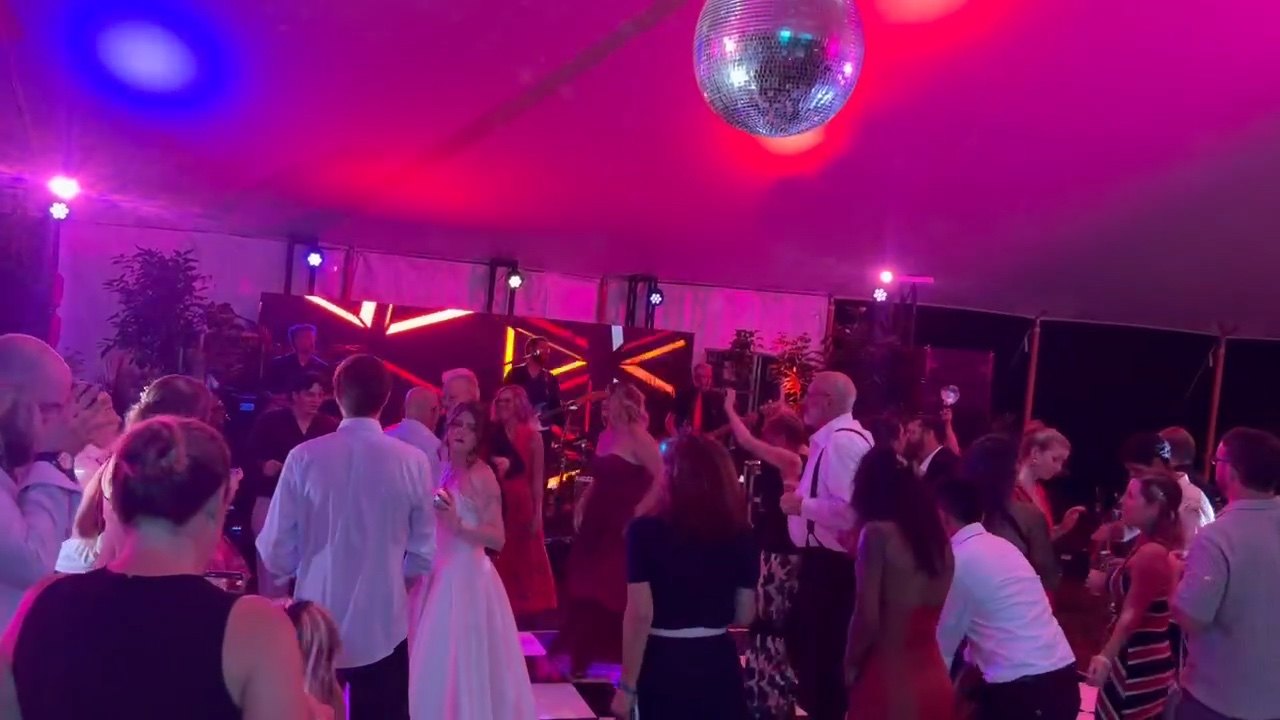Wedding guests filling the dance floor beneath colorful lights while The Chucks perform